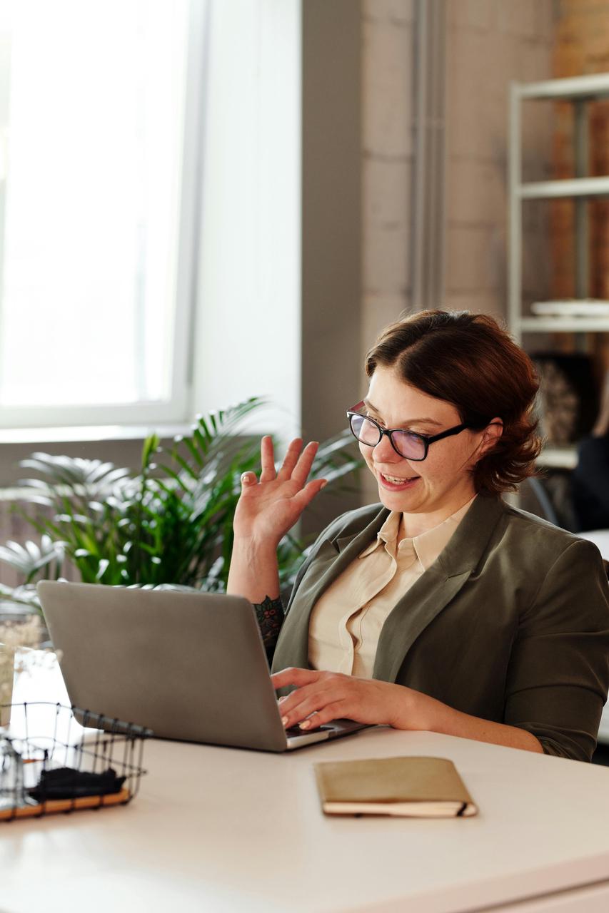 A woman wearing glasses sits at a desk, focused on her laptop, engaged in work or study.